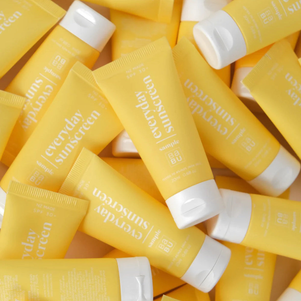 Multiple yellow sunscreen samples with white caps on a white background