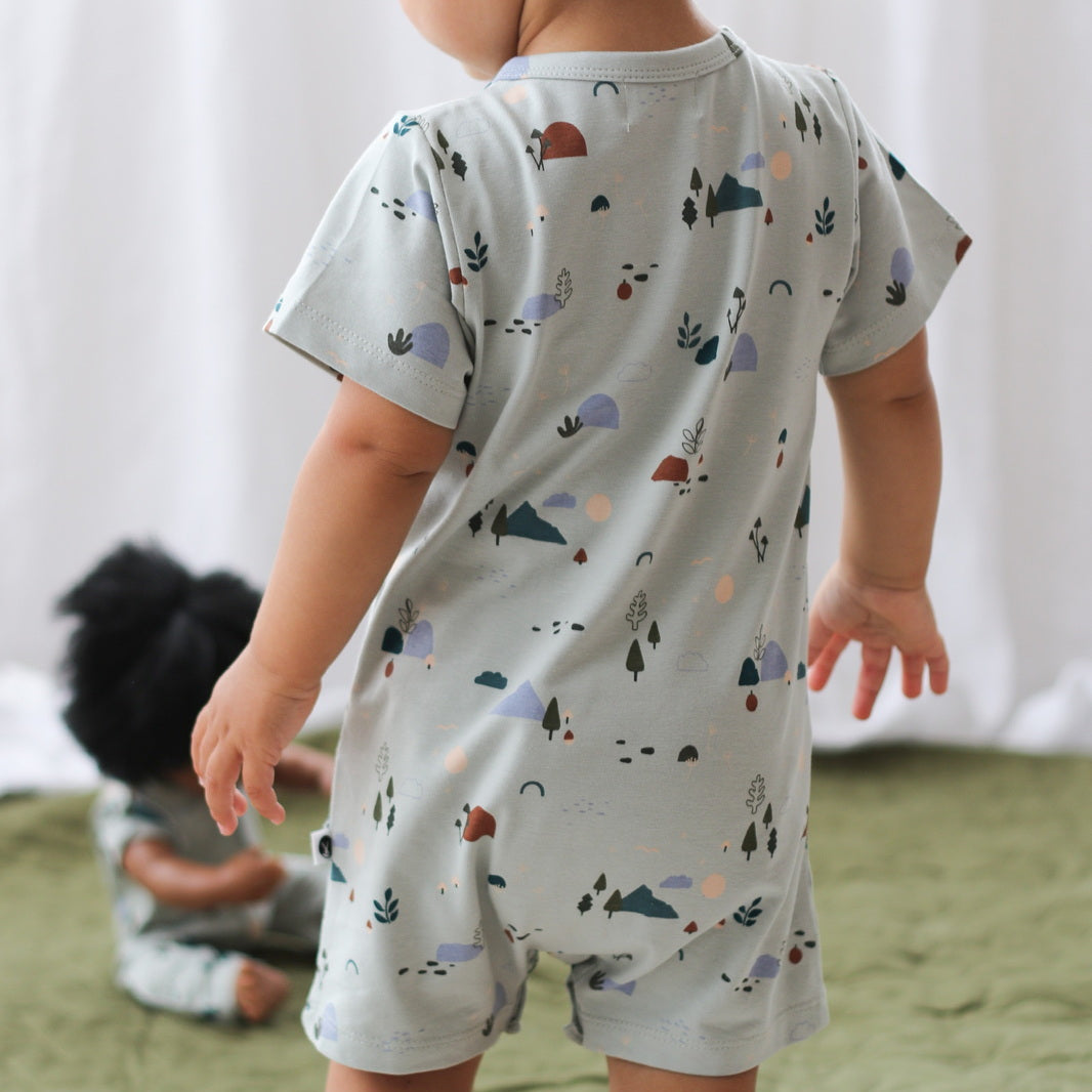 Child wearing a light-colored outfit with animal prints standing on a bed.