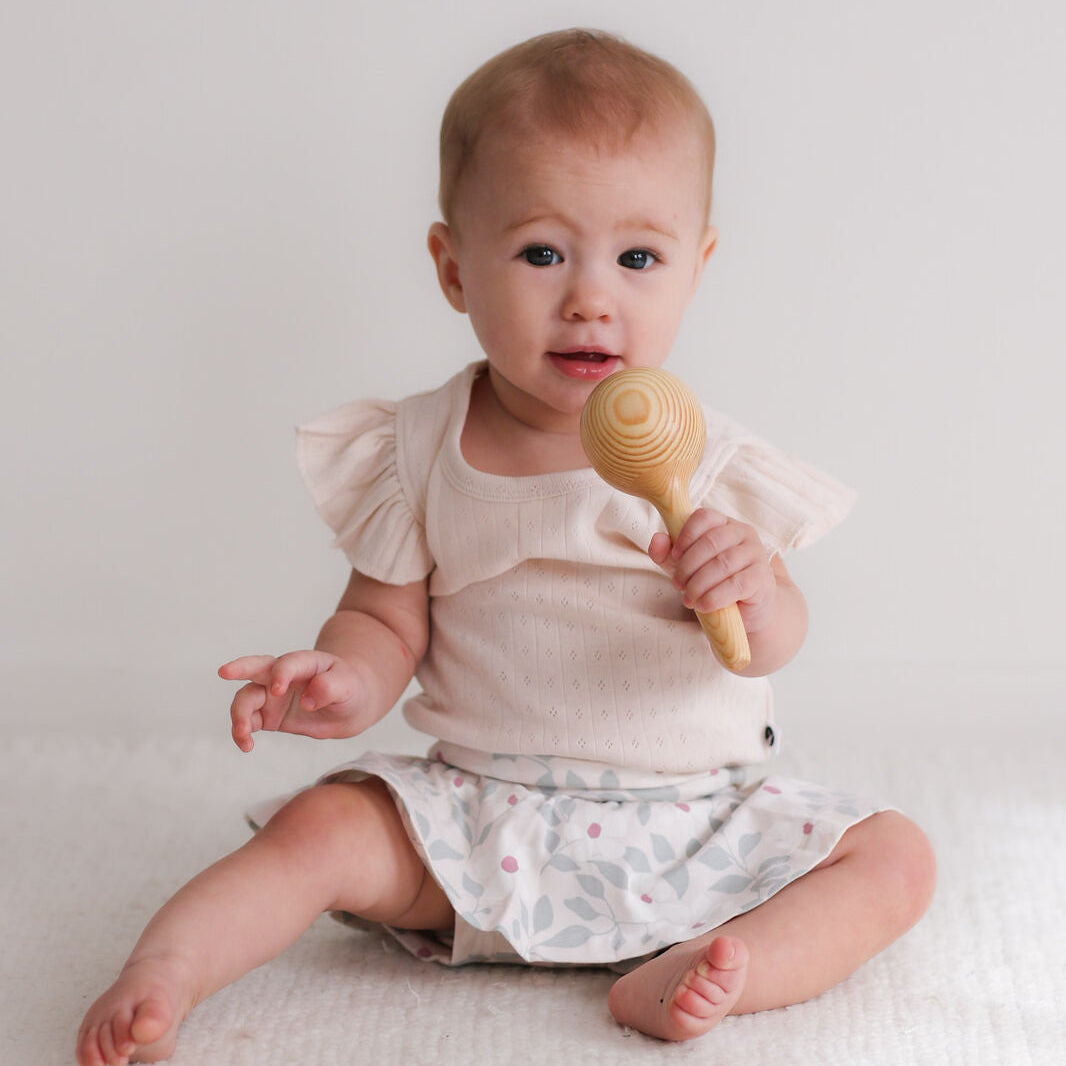 Baby holding a wooden rattle against a plain background