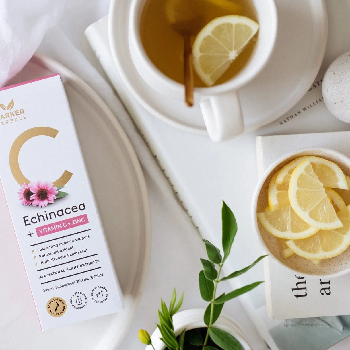 Box of Echinacea + Vitamin C supplement next to a cup of tea with lemon slices on a white surface.