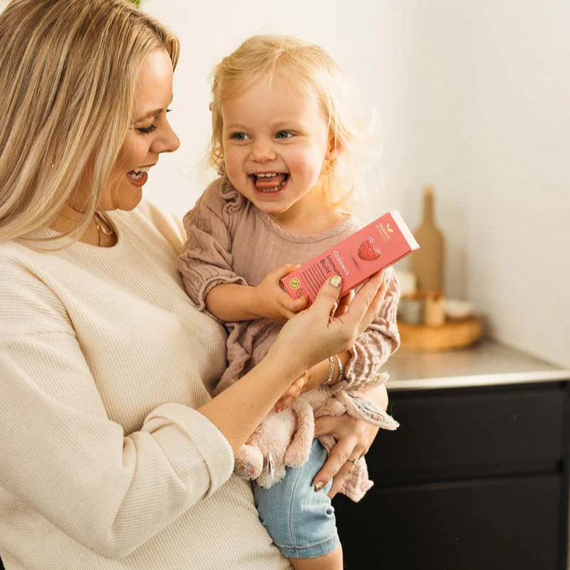 Woman holding a child who is holding a boxed bottle of immune build in a home setting.