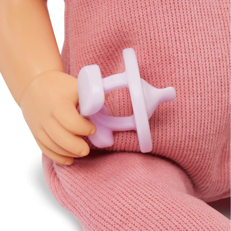 Child's hand holding a pink silicone teether against a pink knitted fabric background
