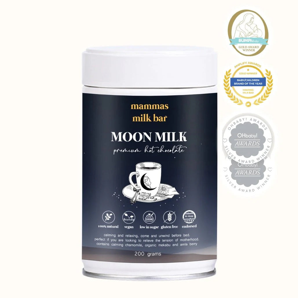 A cylindrical canister of 'Mammas Milk Bar' Moon Milk Premium Hot Chocolate on a light cream background, featuring award badges on the right.