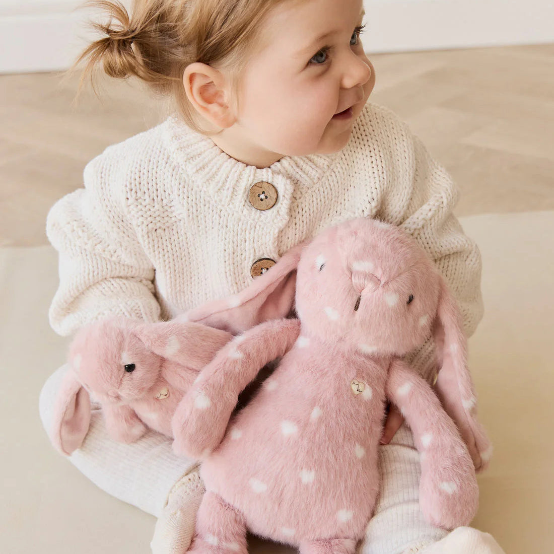 Child holding a pink plush toy with white polka dots on a light background