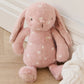 Pink plush bunny toy with white polka dots on a wooden floor.