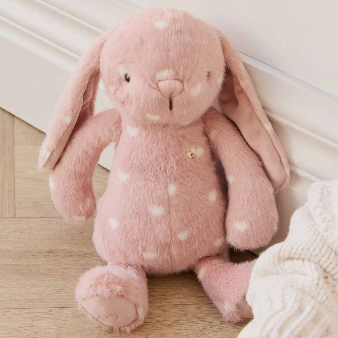 Pink plush bunny toy with white polka dots on a wooden floor.