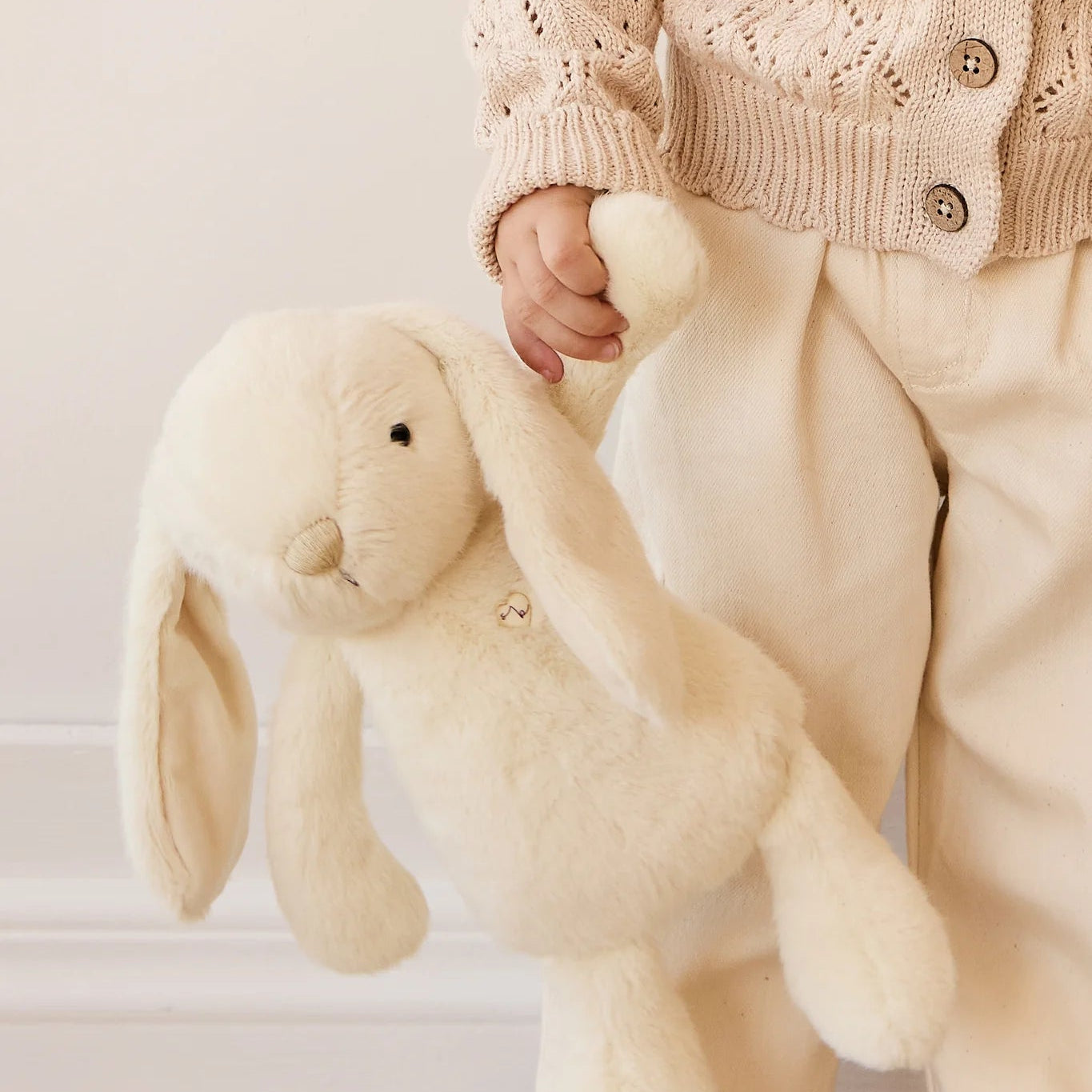 Person holding a large cream-colored plush bunny toy indoors.