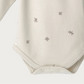 Beige baby bodysuit with star patterns showing domes on a light grey background