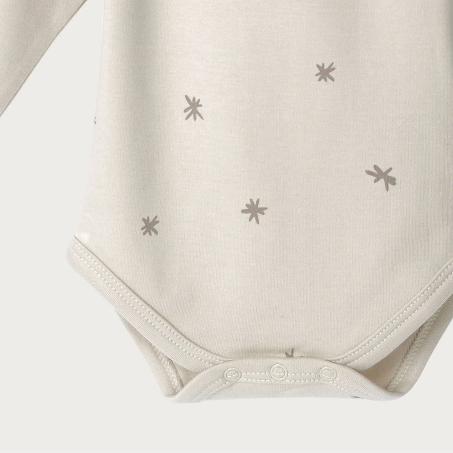 Beige baby bodysuit with star patterns showing domes on a light grey background