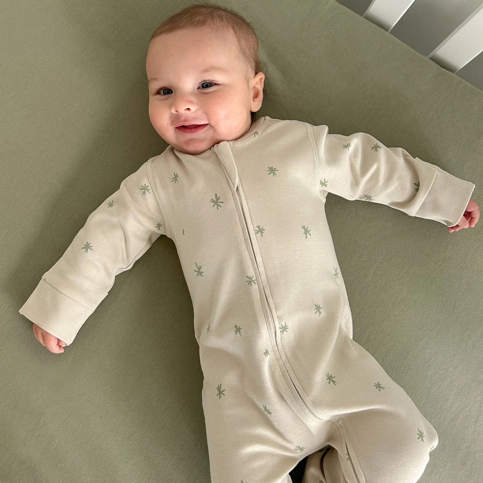 Baby in a cream-colored onesie with small patterns lying on a green surface.