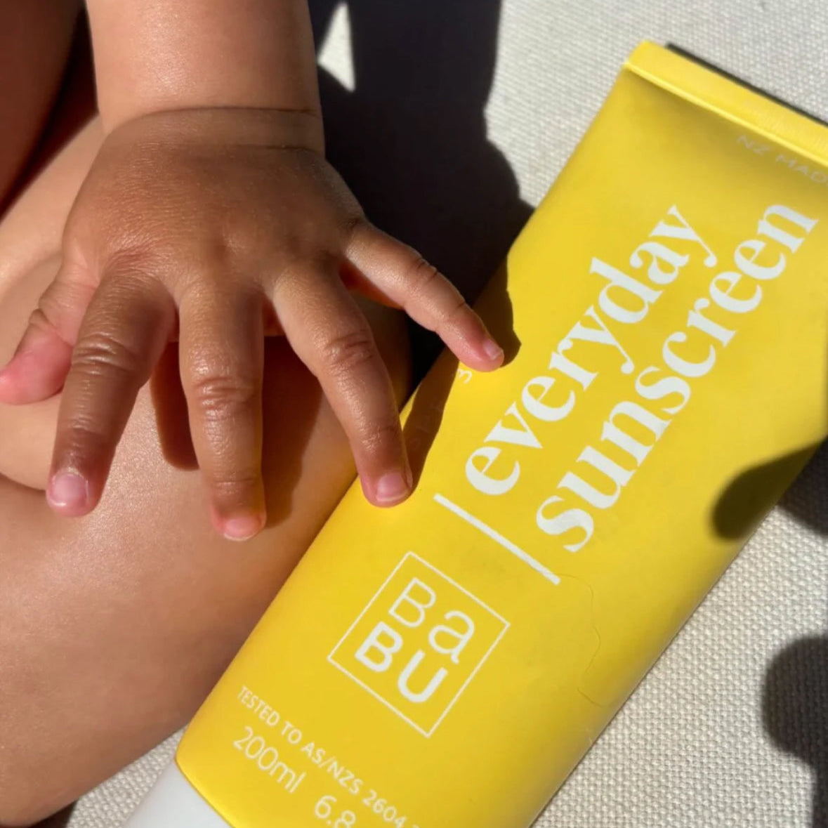 Yellow sunscreen bottle labeled 'everyday sunscreen' held by a child's hand.