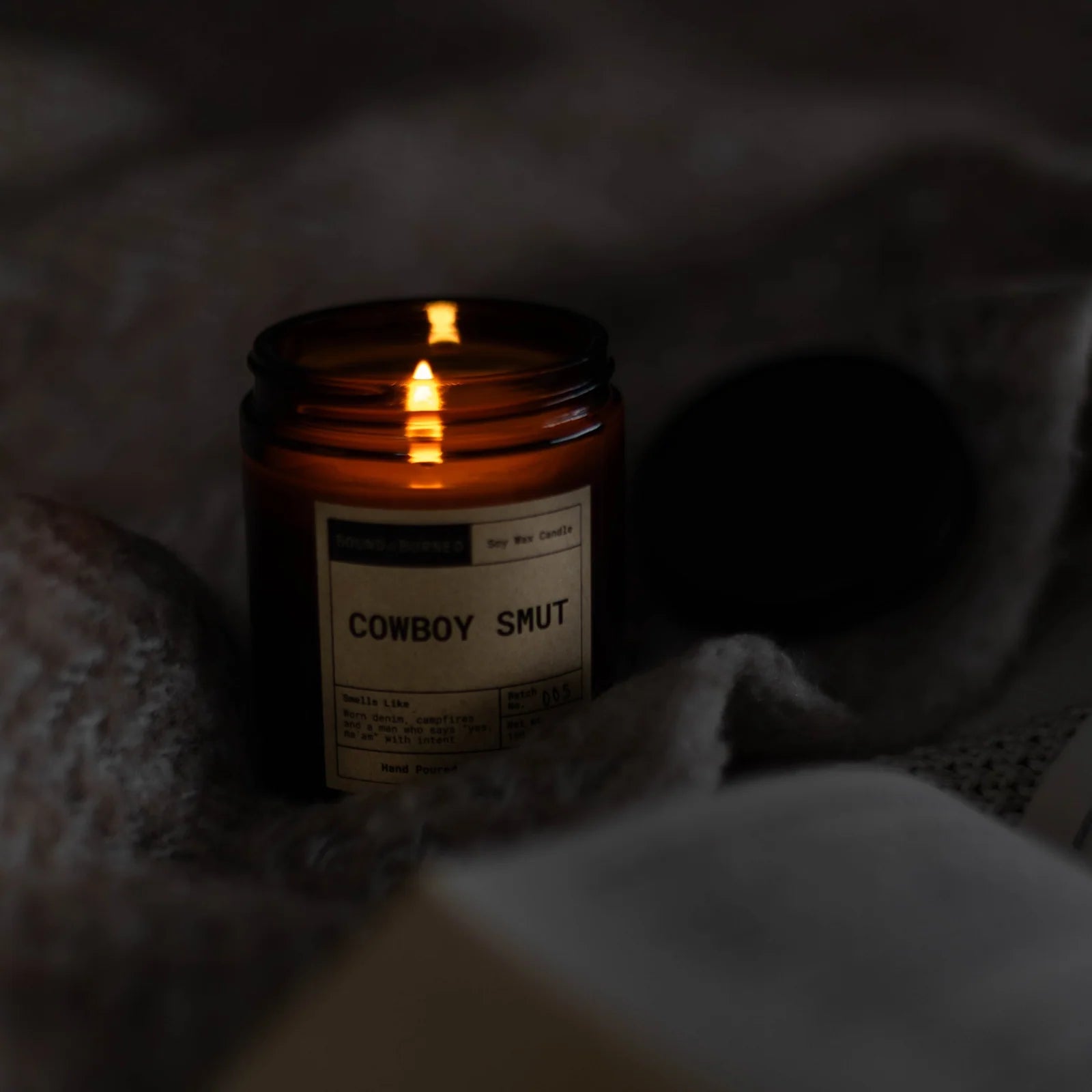 Candle labeled 'Cowboy Smut' in a dark setting