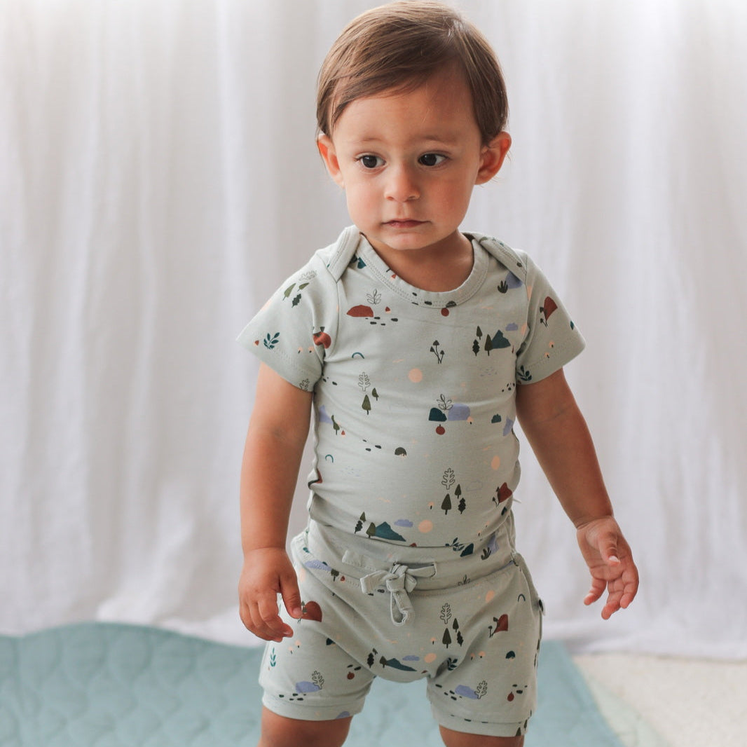 Child wearing a light blue outfit with nature-themed print on a white background