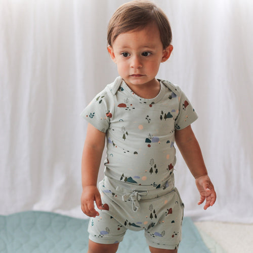 Child wearing a light blue outfit with nature-themed print on a white background