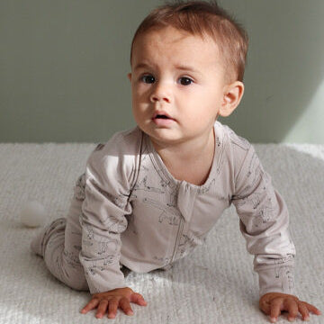 Baby in a light gray onesie crawling on a white blanket with a neutral background