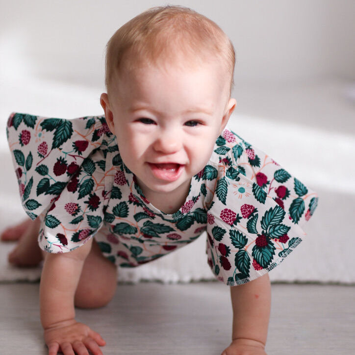 Baby crawling on a light-colored floor wearing a floral outfit.