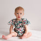 Baby wearing a floral onesie sitting on a white blanket