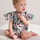 Baby wearing a floral romper sitting on a light-colored blanket.