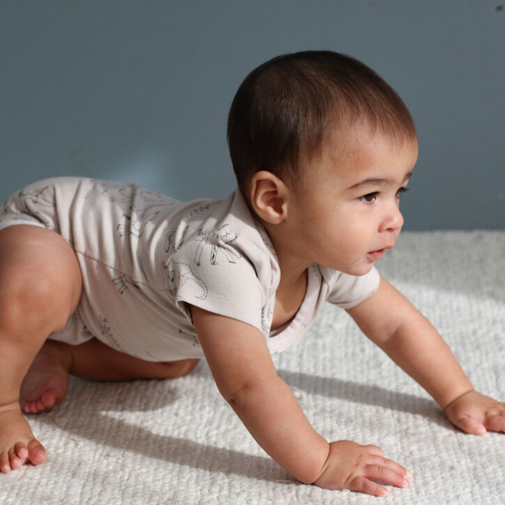 Baby in a light-colored outfit crawling on a textured surface with a neutral background