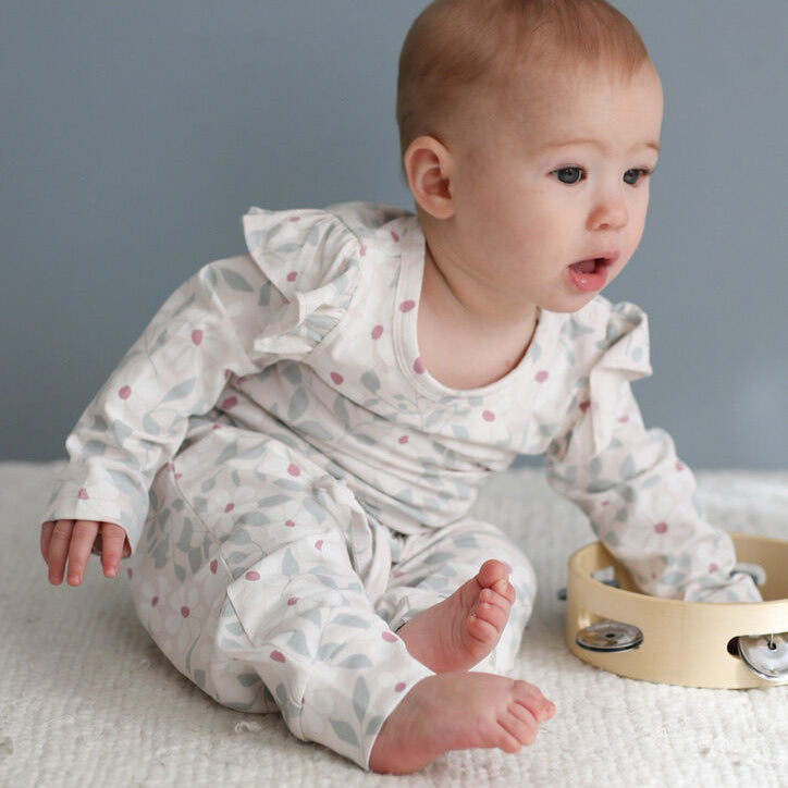 Baby in a white outfit with ruffles sitting on a textured surface with a gray background