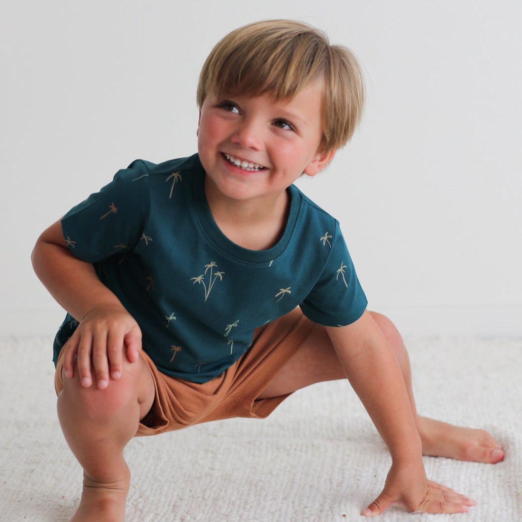 Child wearing a blue shirt and brown shorts sitting on a white surface