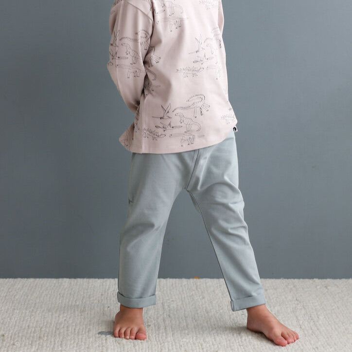 Child wearing a light grey long-sleeve shirt and light blue pants against a grey background