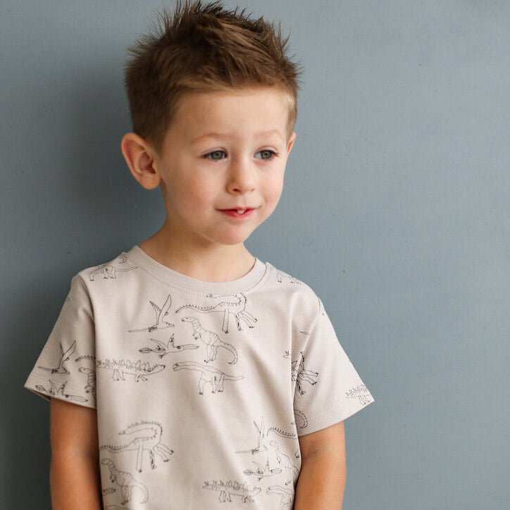 Young boy wearing a light-colored t-shirt with graphics against a gray background