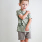 Young boy wearing a green t-shirt and gray shorts on a white background