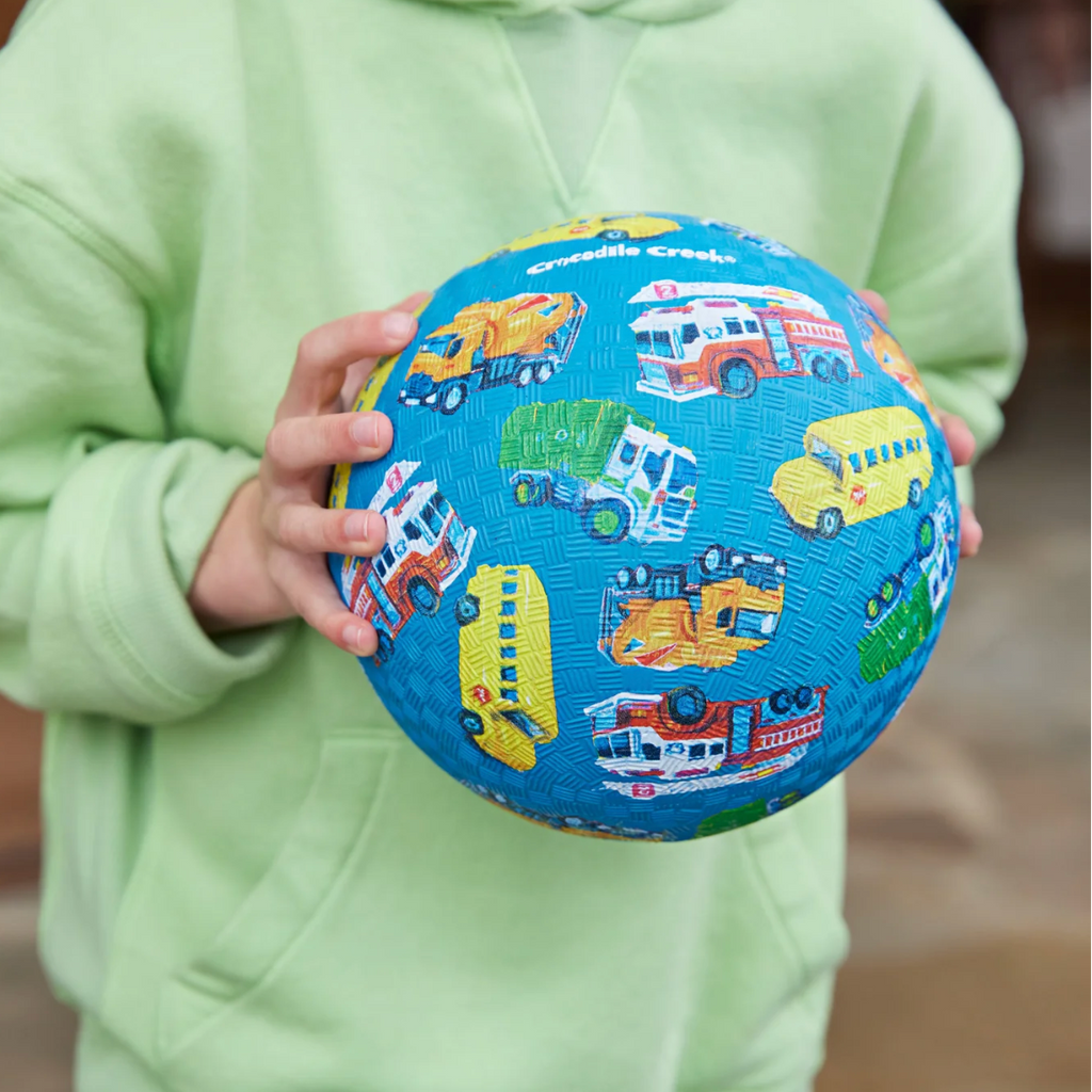 Child holding a blue ball with vehicle patterns against a blurred background