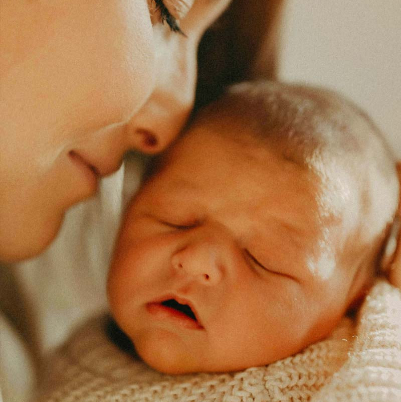 Close-up of a woman and a baby wrapped in a textured blanket.