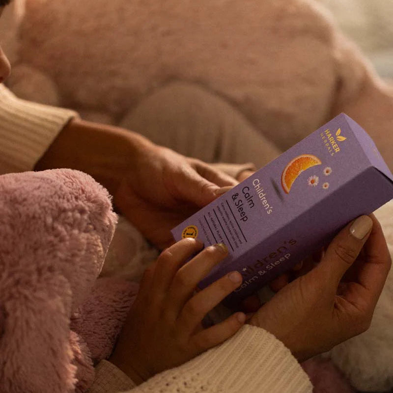 Person holding a purple children's supplement package with a soft, warm background.