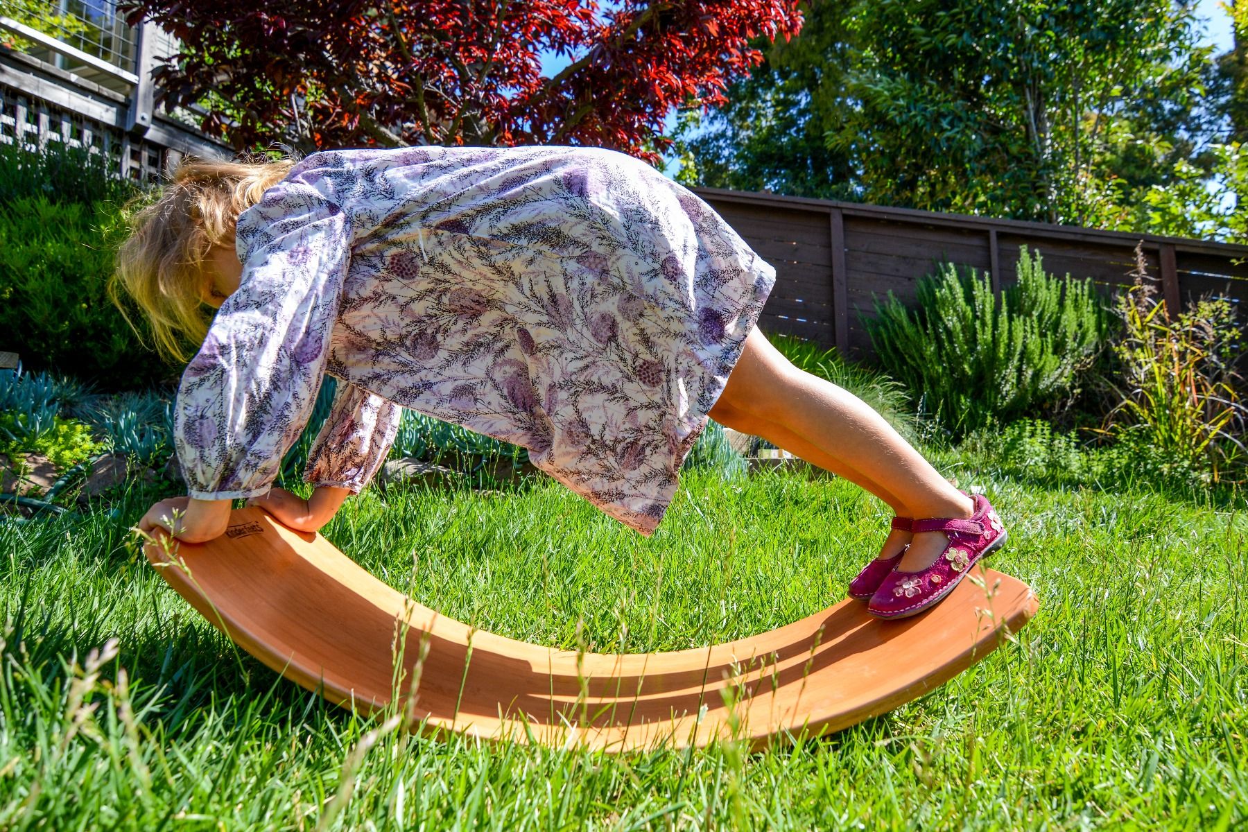 Child playing on a wooden kinderboard in a grassy backyard