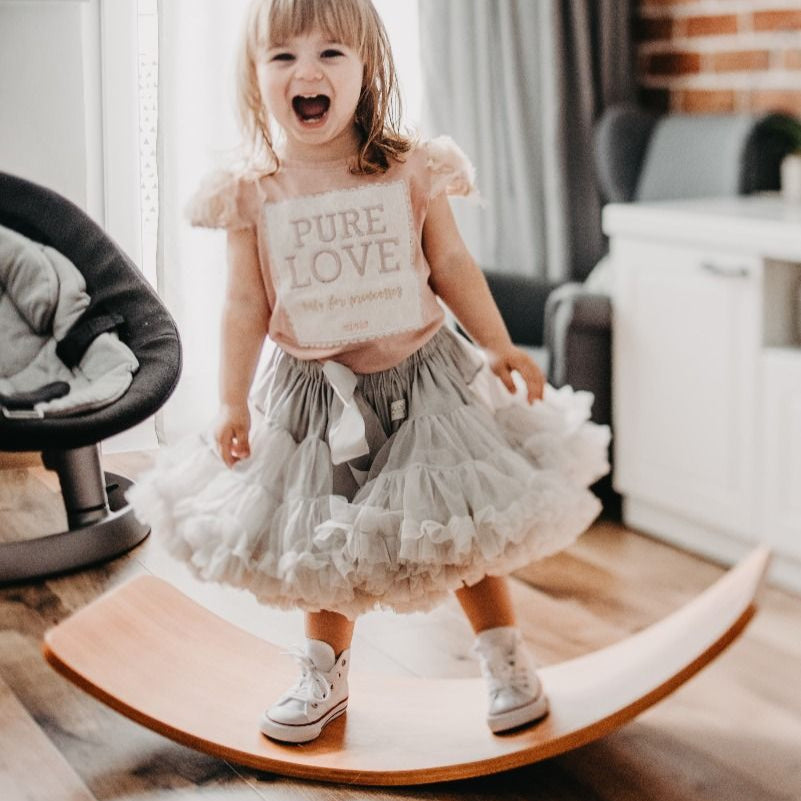 Child standing on a wooden balance board in a home setting