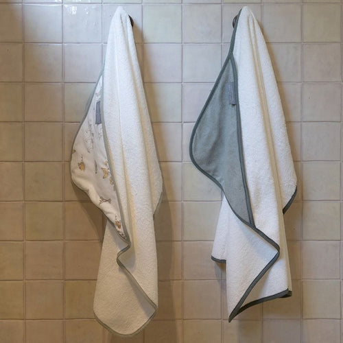 Two hooded towels hanging on a tiled wall.