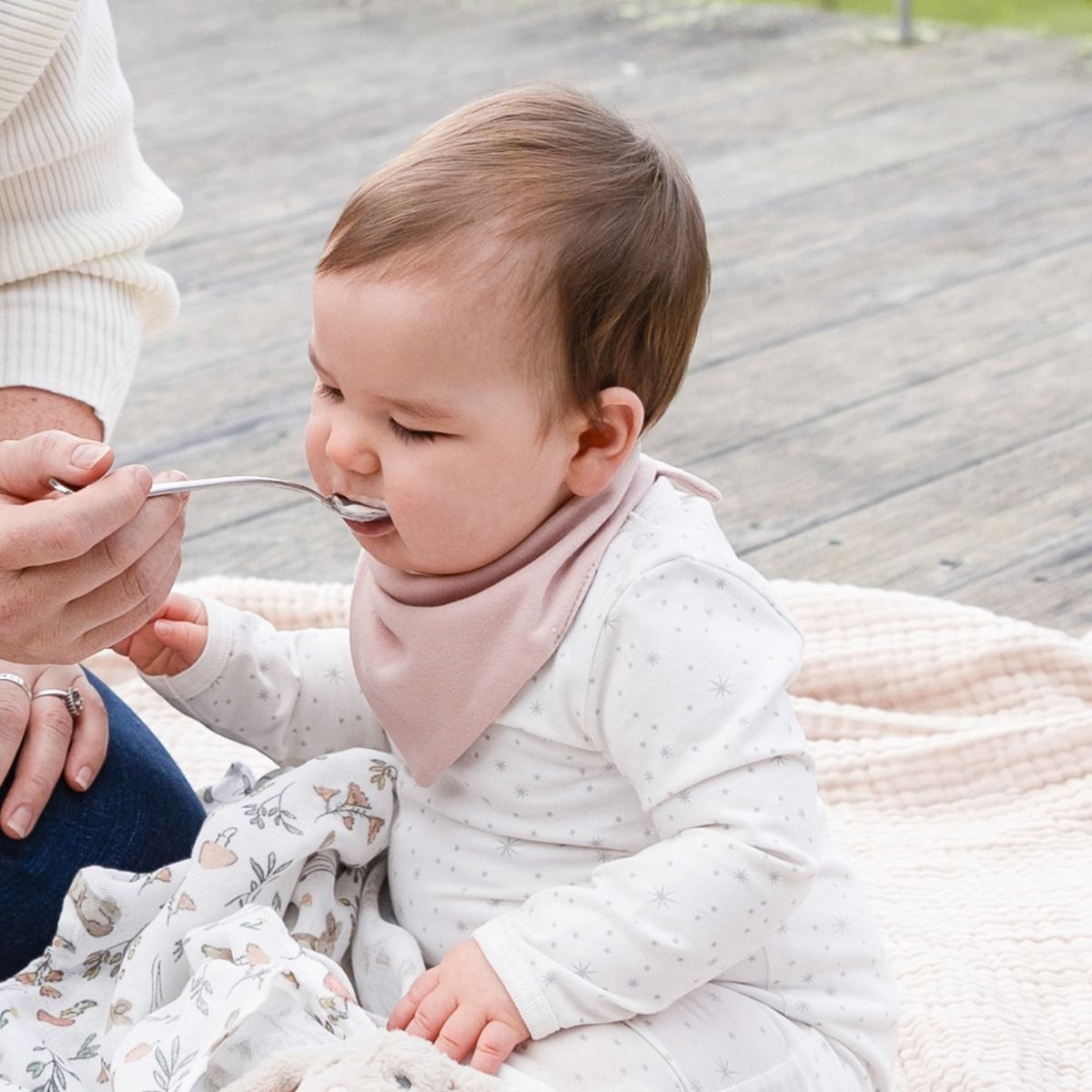 Baby being fed with a spoon by an adult outdoors