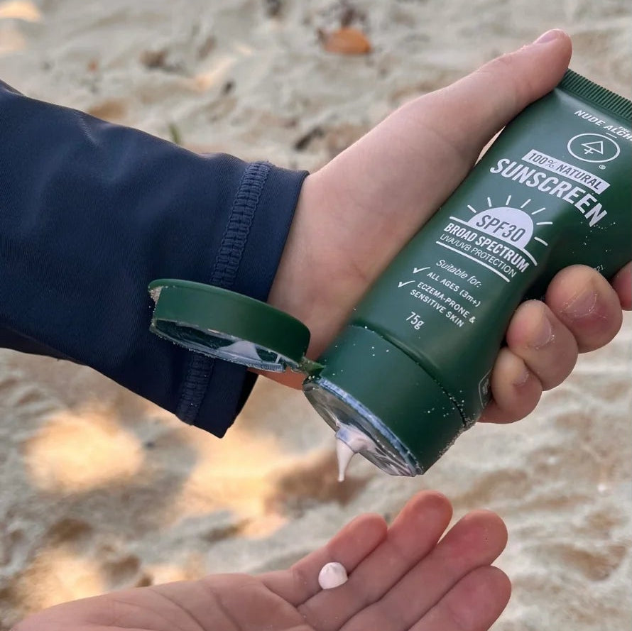 Sunscreen application on a beach with a person applying sunscreen to another person's arm.