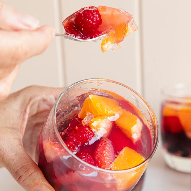 Glass of fruit and strawberry gusty gummy jelly with a spoonful of fruit above it, on a light background