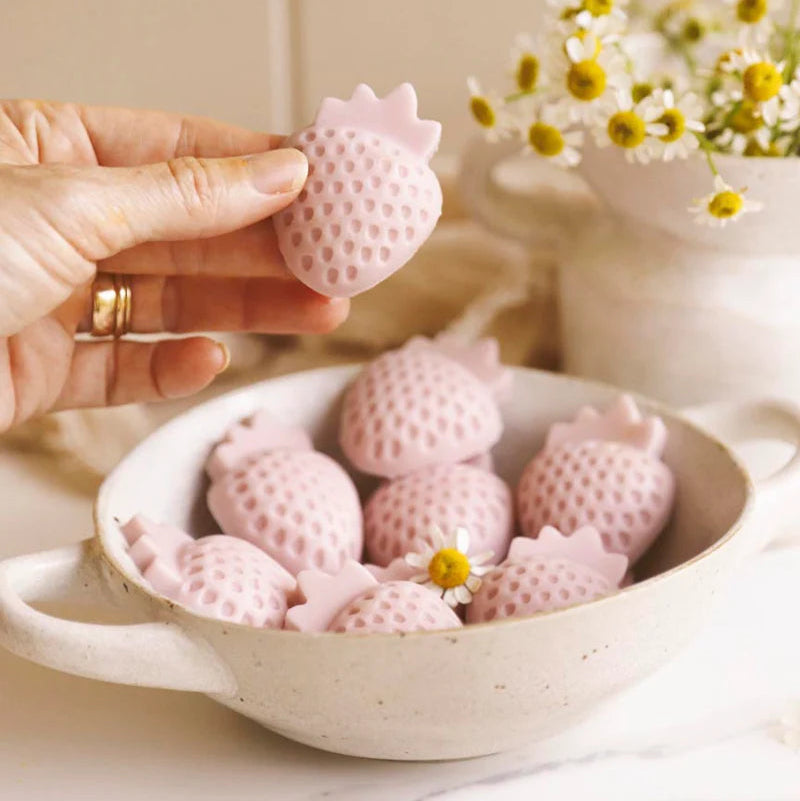 Pink strawberry-shaped yoghurt gusty gummies in a bowl with a hand holding one, on a light background.