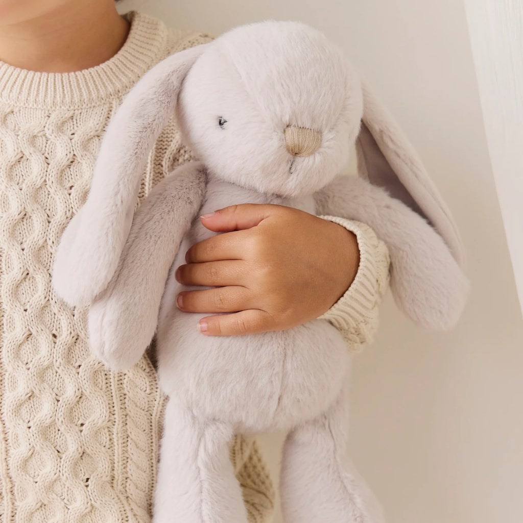 Child holding a plush bunny toy against a neutral background