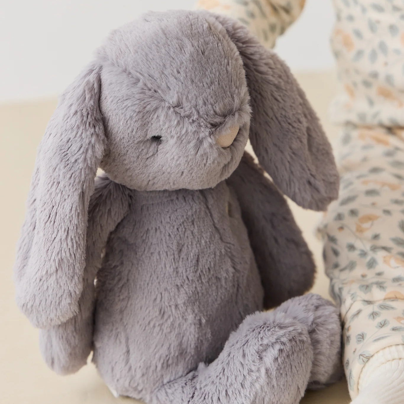 Gray plush bunny toy on a light surface with a blurred background