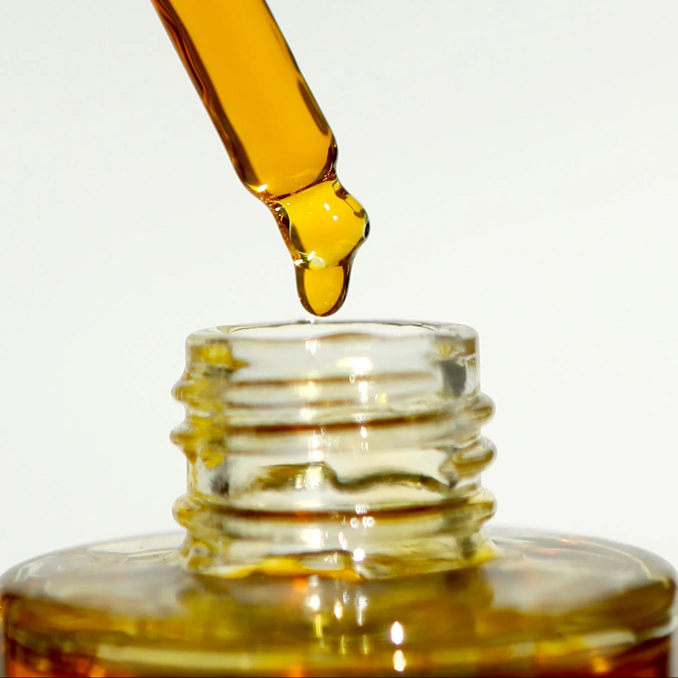 Close-up of a dropper with yellow liquid being added to a glass container.