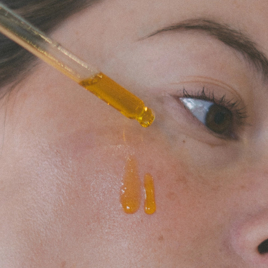 Close-up of a dropper with yellow liquid being applied to a person's skin.