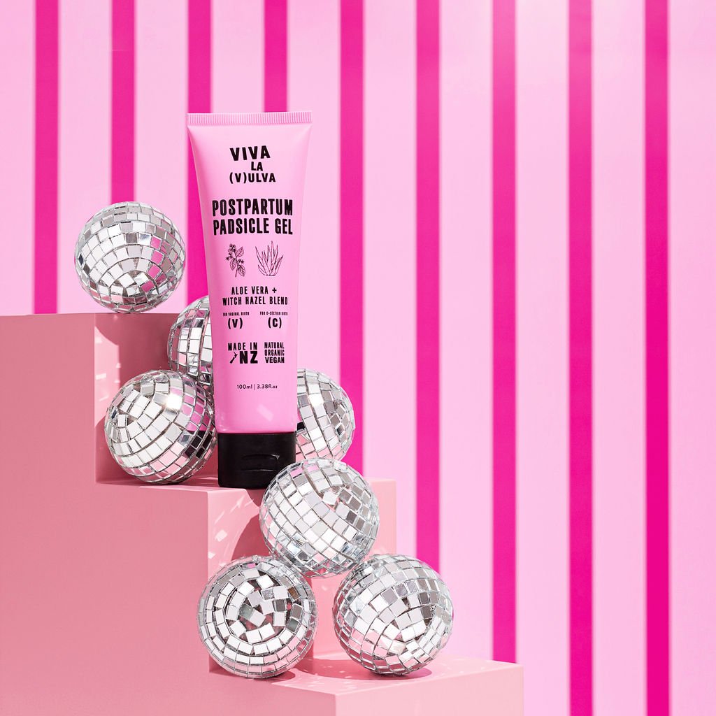 A tube of Viva La Vulva Postpartum Padsicle Gel displayed alongside several disco balls on a pink and white striped background.
