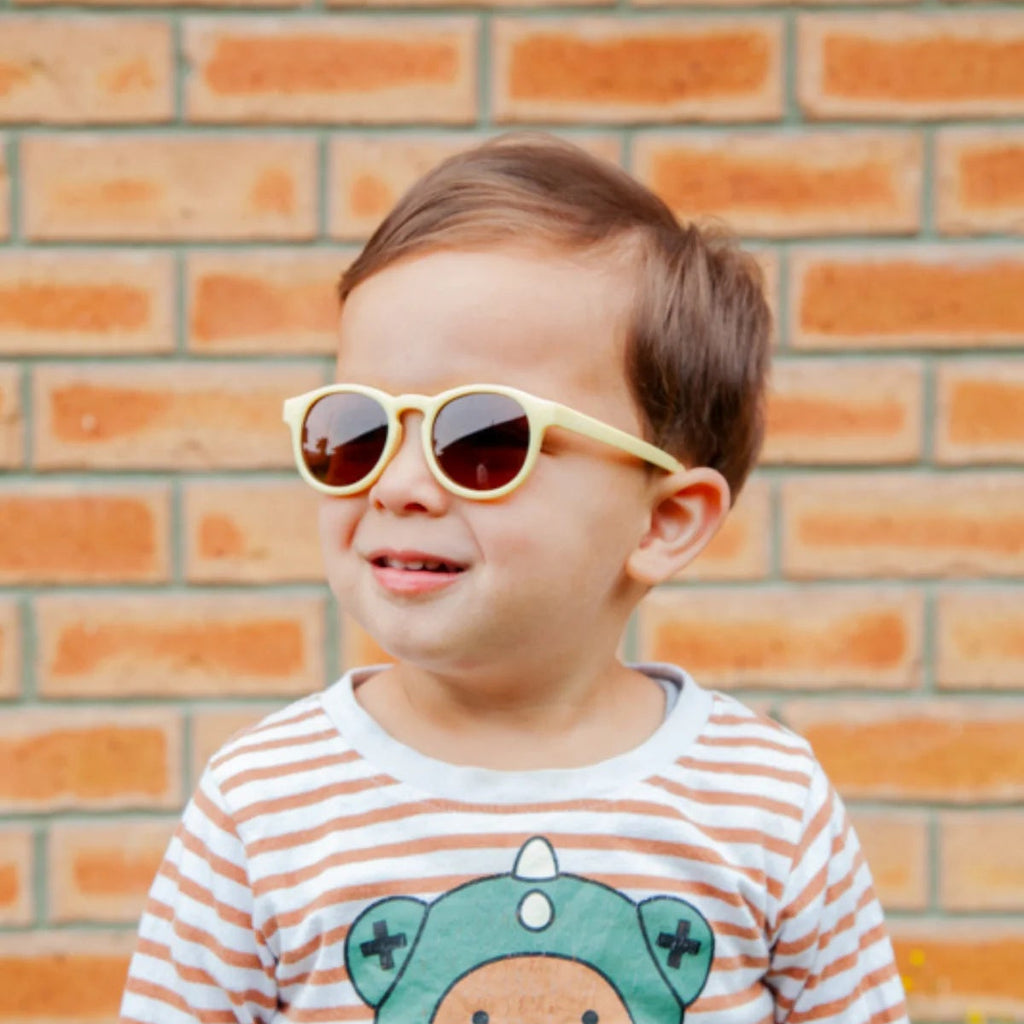 Child wearing sunglasses and a striped shirt with a bear design in front of a brick wall.